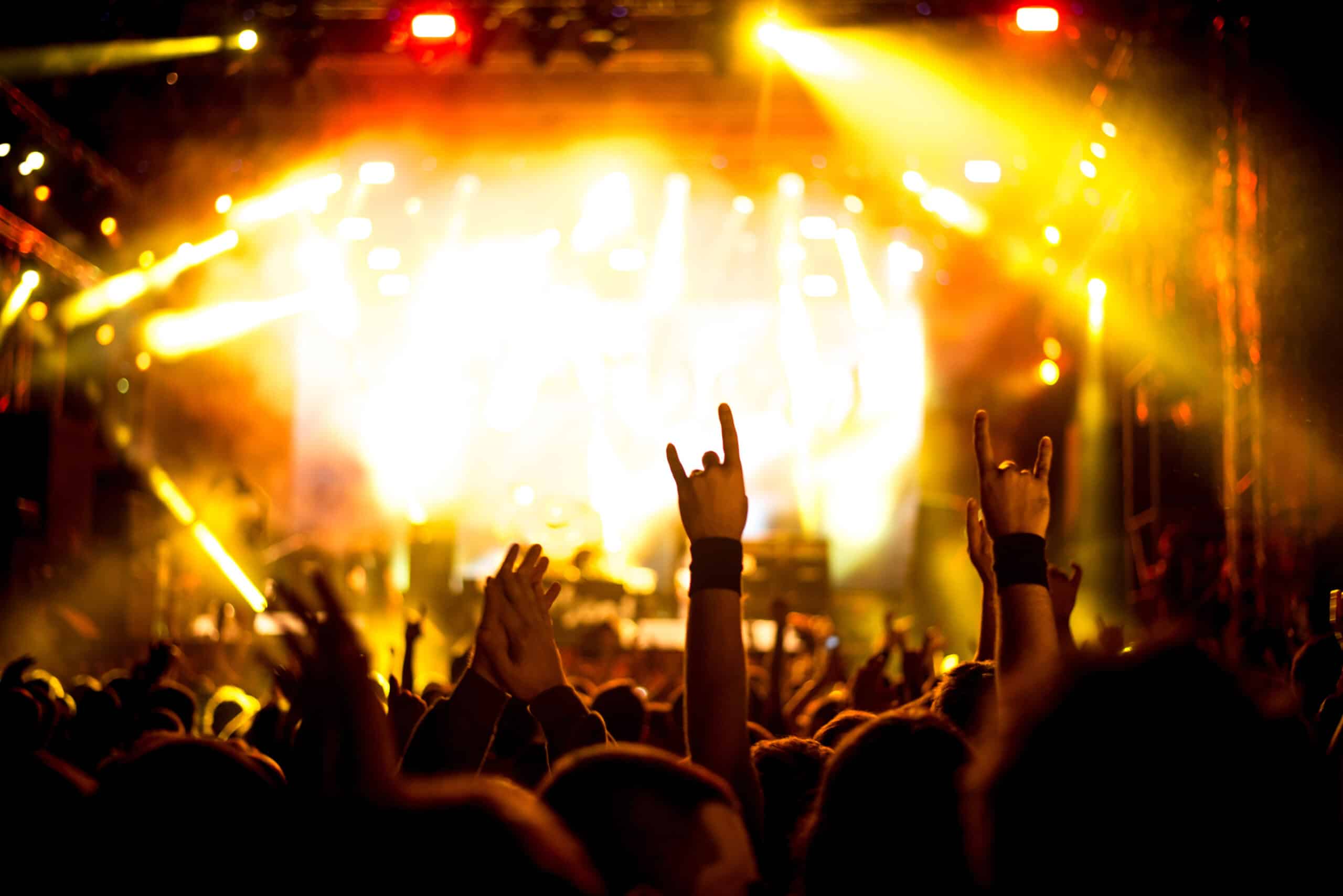 A crowd at a concert raises hands and makes the 