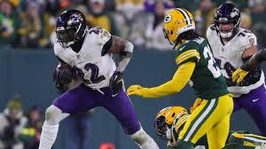 A Baltimore Ravens player runs with the football while being pursued by Green Bay Packers defenders during an NFL game.