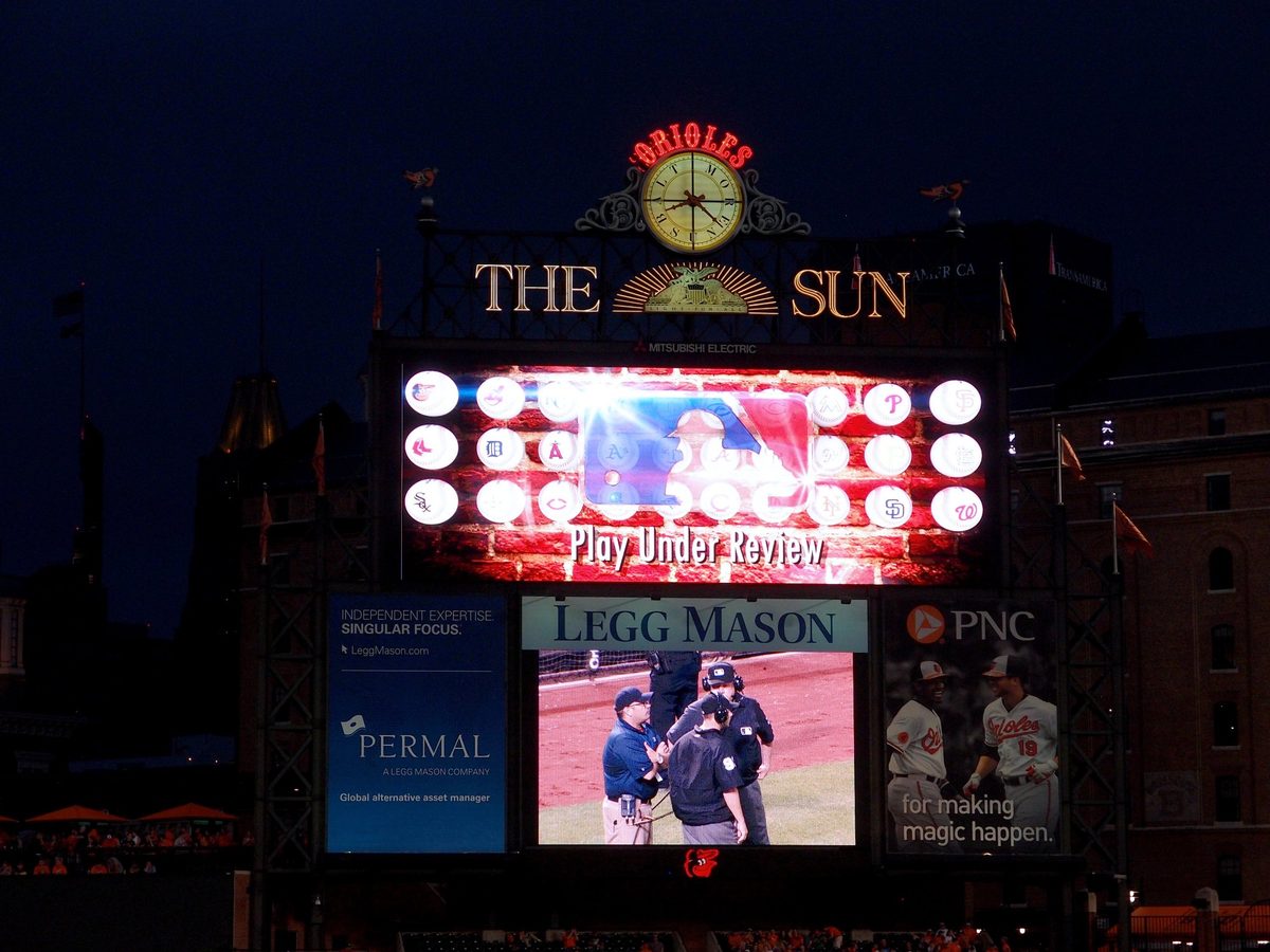 The iconic Camden Yards scoreboard lit up at night with the Orioles clock and Baltimore Sun sign